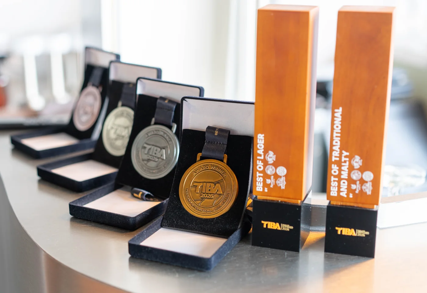 เหรียญ TIBA 2026 ของจริง 4 เหรียญ ทอง 1 เงิน 2 ทองแดง 1 กับถ้วย Best of Lager และ Best of Traditional and Malty ตั้งบนเคาน์เตอร์ร้าน Underdog